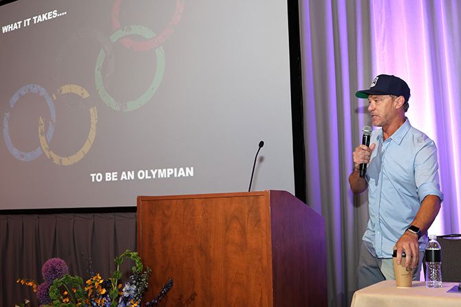 A man in a baseball cap and casual clothing giving a speech on stage