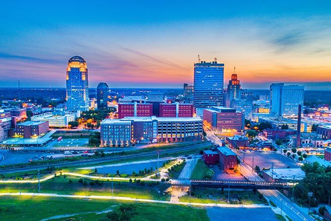 Chairman’s Column: Finishing Strong and Looking Ahead. A vibrant cityscape at dusk, featuring modern skyscrapers and colorful lights. The sunset paints the sky in hues of orange and blue, creating a serene ambiance.