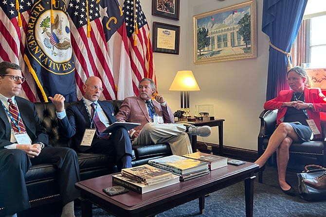 NCADA Leadership Advocates for Dealers; Four people sit in a formal office with U.S. flags and a seal behind them. They appear engaged in discussion. The room has framed art and certificates on the walls.
