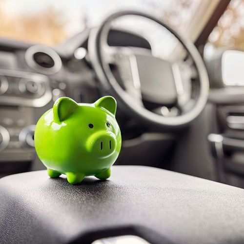 Driving North Carolina’s Economy; A green piggy bank sits on a car's armrest in the front seat. The car's interior is blurred, suggesting themes of savings and travel.