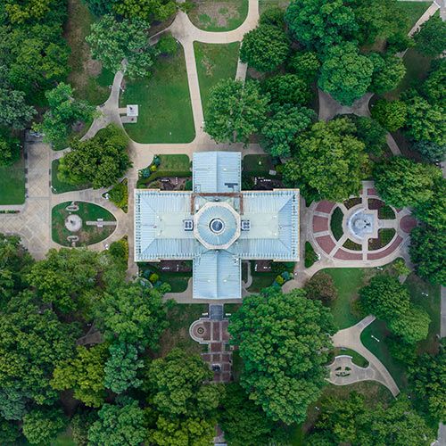 NCADA Strengthens Dealer Protections with New Franchise Legislation; Aerial view of a symmetrical building surrounded by lush green trees and winding pathways in a park, exuding a serene and orderly atmosphere.